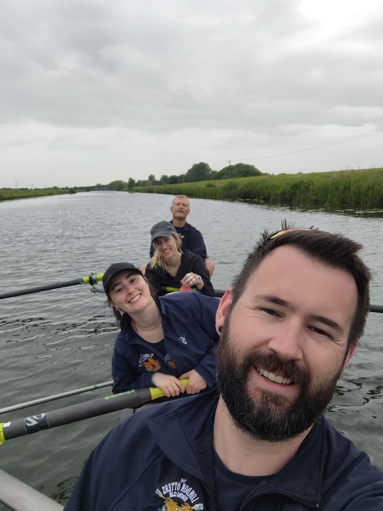 Jamie and three crewmates in a boat on the water, oars out, early morning.