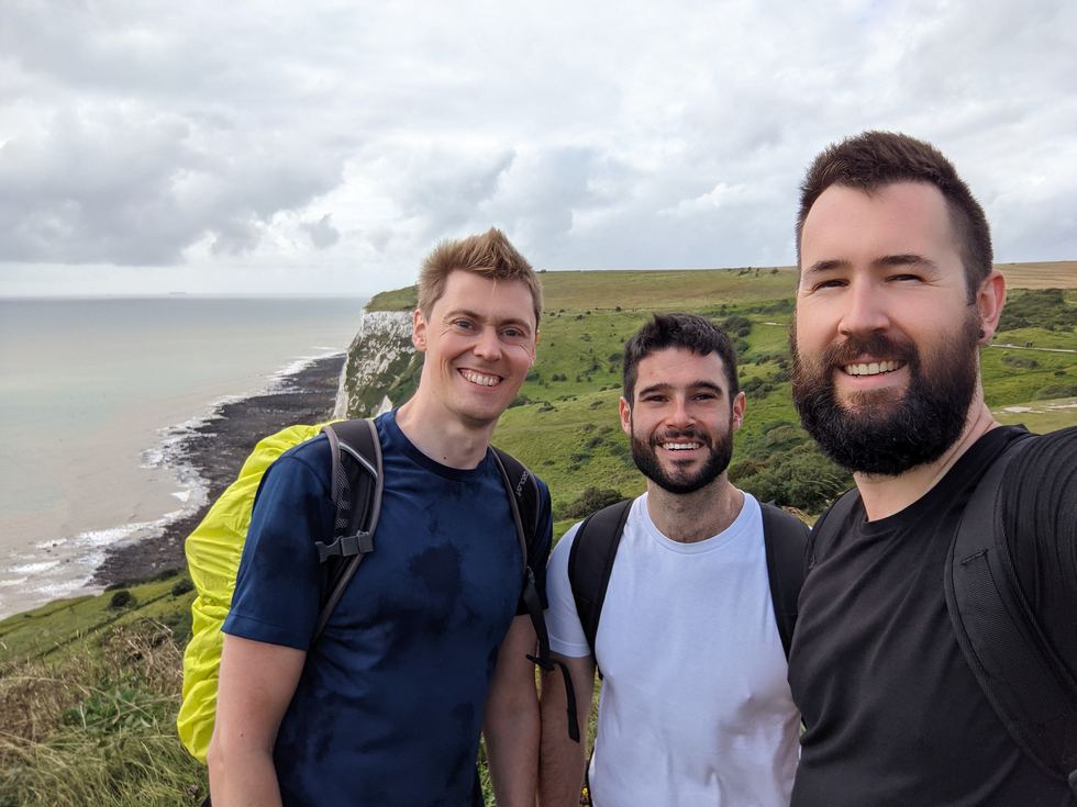 Jamie and two friends on the coast path above the white cliffs, packs on, weather coming in.